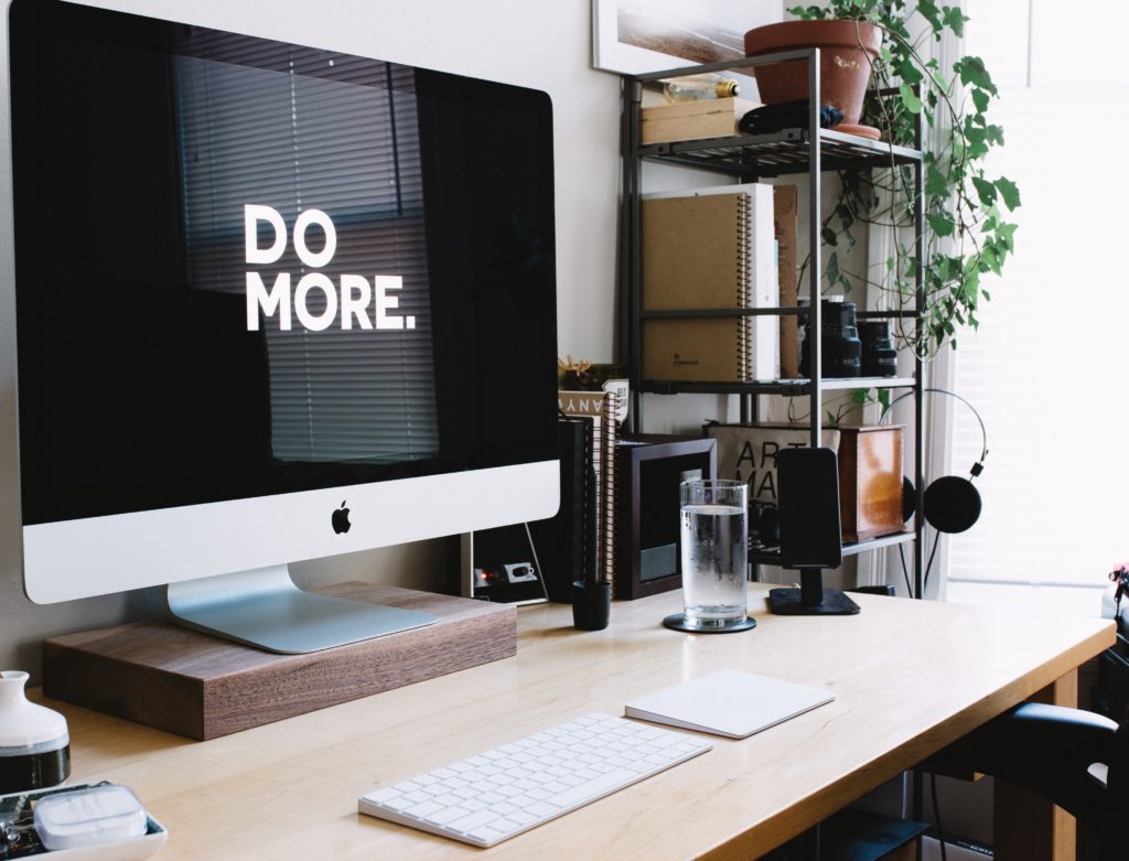 a home office desk with a computer, keyboard and a screen that says do more on it